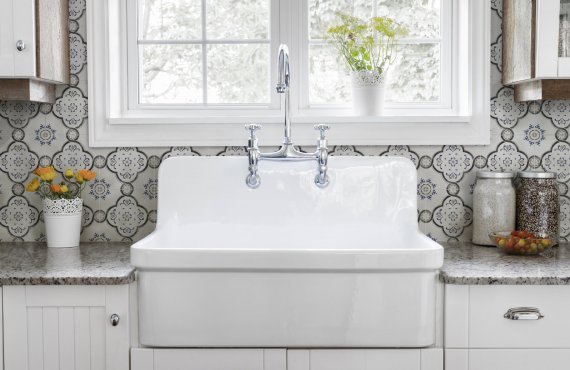 Kitchen interior with large rustic white porcelain sink and granite stone countertop under sunny window